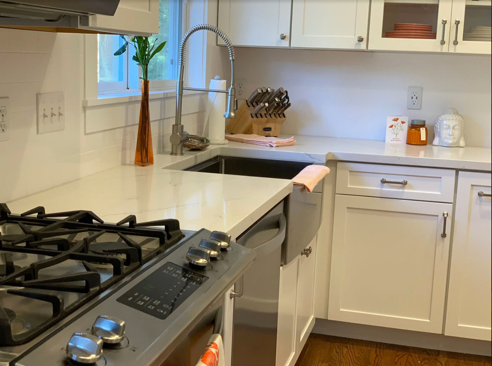 Mid-sized country eat-in kitchen in Other with a farmhouse sink, raised-panel cabinets, white cabinets, quartz benchtops, white splashback, stainless steel appliances, with island, brown floor and white benchtop.