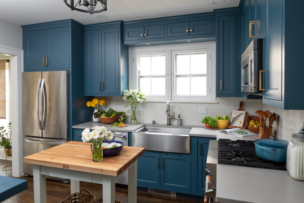 Modelo de cocina de estilo de casa de campo de tamaño medio con despensa, puertas de armario azules, salpicadero de azulejos de cerámica, suelo vinílico, suelo marrón y encimeras blancas
