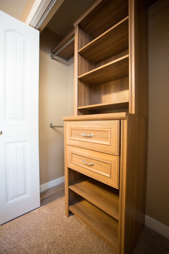 Mid-sized traditional gender-neutral built-in wardrobe in Edmonton with recessed-panel cabinets, medium wood cabinets, carpet and beige floor.