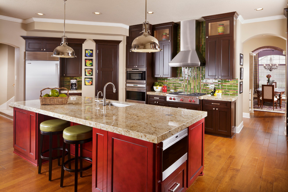 This is an example of a large traditional l-shaped kitchen in Houston with an undermount sink, recessed-panel cabinets, dark wood cabinets, granite benchtops, green splashback, glass tile splashback, stainless steel appliances, medium hardwood floors, with island, brown floor and beige benchtop.