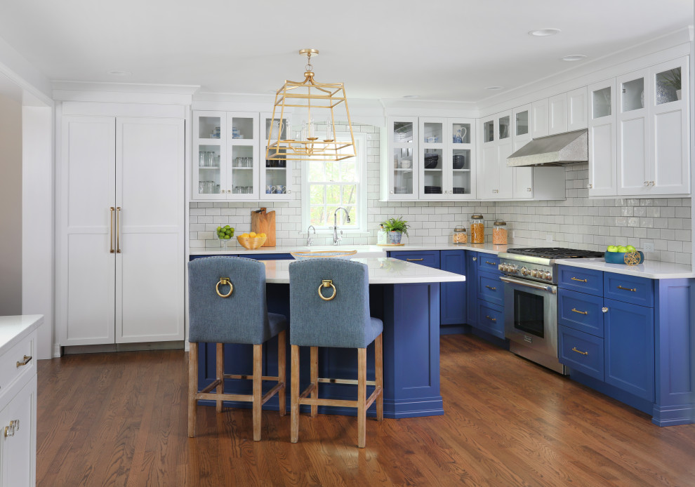 Large transitional l-shaped medium tone wood floor and brown floor eat-in kitchen photo in Chicago with a farmhouse sink, quartz countertops, white backsplash, paneled appliances, an island, white countertops, white cabinets, glass tile backsplash and shaker cabinets