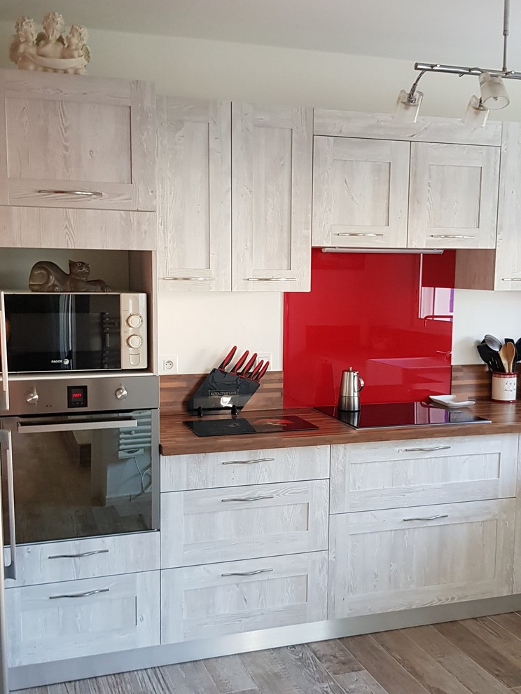 This is an example of a mid-sized midcentury l-shaped separate kitchen in Other with a farmhouse sink, beaded inset cabinets, distressed cabinets, laminate benchtops, red splashback, mirror splashback, stainless steel appliances, laminate floors, no island, brown floor and brown benchtop.