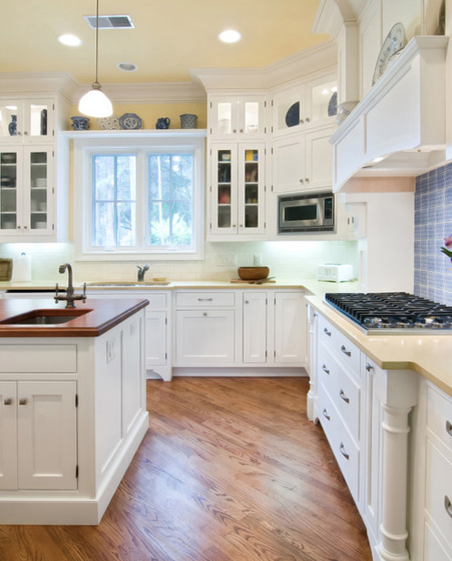 Transitional l-shaped medium tone wood floor kitchen photo with an undermount sink, shaker cabinets, white cabinets, white backsplash, stainless steel appliances and an island