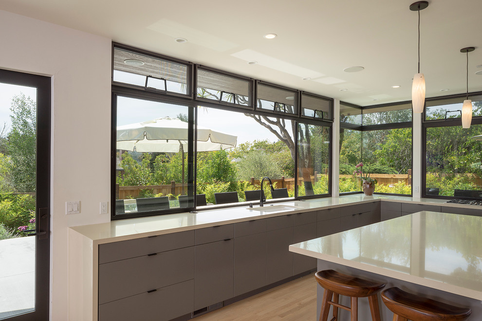 Photo of a large contemporary l-shaped open plan kitchen in San Francisco with flat-panel cabinets, grey cabinets, quartz benchtops, stainless steel appliances, light hardwood floors, with island and an undermount sink.