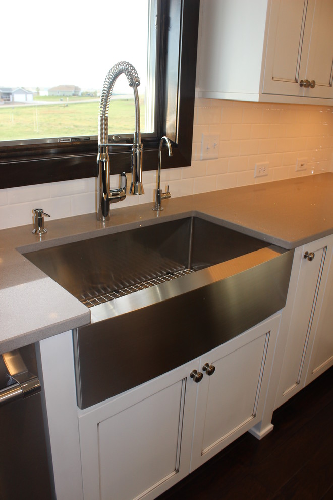 Inspiration for a large transitional l-shaped dark wood floor enclosed kitchen remodel with a farmhouse sink, shaker cabinets, white cabinets, quartz countertops, white backsplash, subway tile backsplash, stainless steel appliances and an island