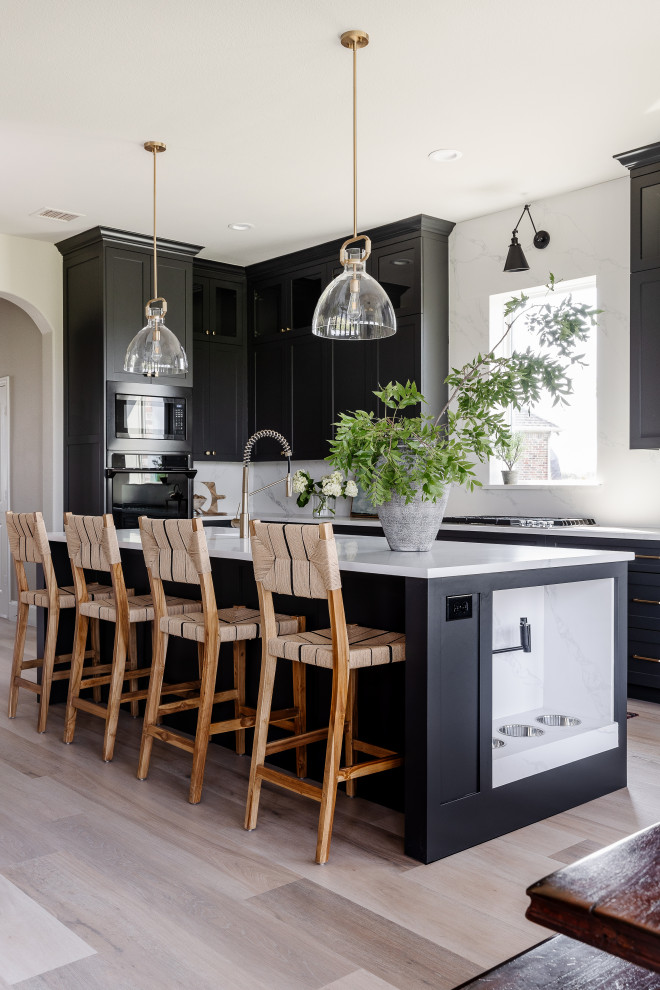Design ideas for a large transitional l-shaped eat-in kitchen in Dallas with a single-bowl sink, shaker cabinets, black cabinets, quartz benchtops, white splashback, engineered quartz splashback, black appliances, vinyl floors, with island, beige floor and white benchtop.