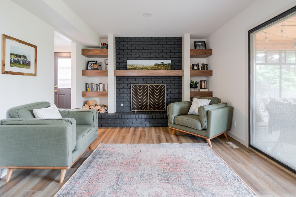 This is an example of a large midcentury open concept family room in Calgary with white walls, laminate floors, a standard fireplace, a brick fireplace surround, no tv and brown floor.
