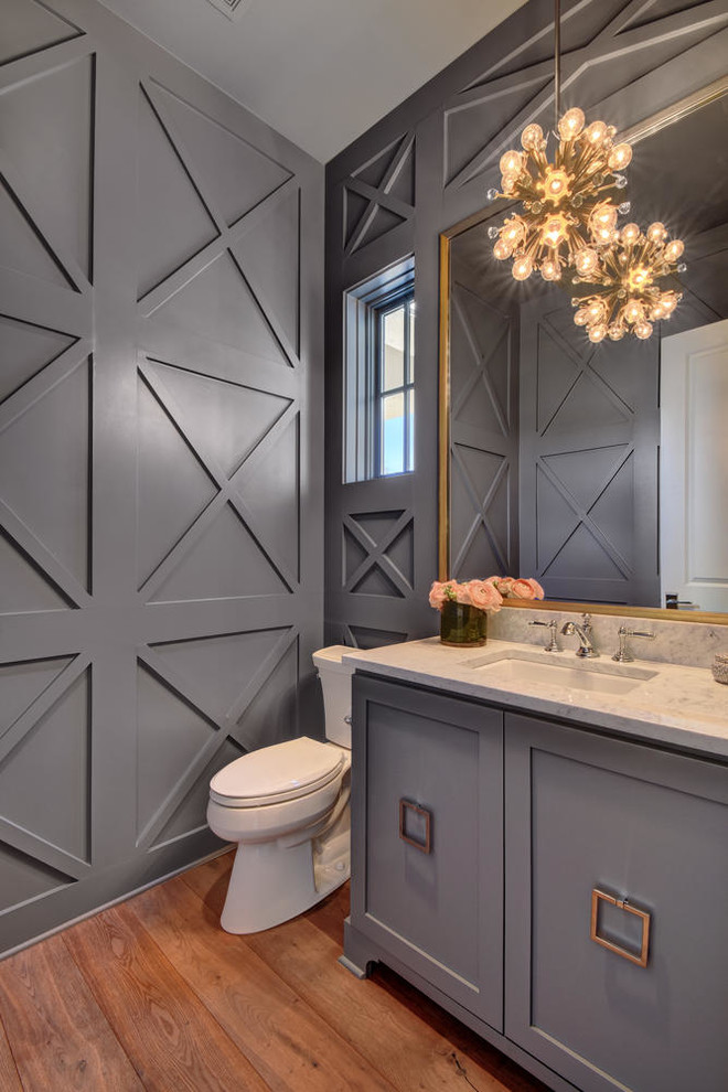 Inspiration for a large transitional powder room in Austin with grey cabinets, a two-piece toilet, grey walls, an undermount sink, marble benchtops, furniture-like cabinets and medium hardwood floors.