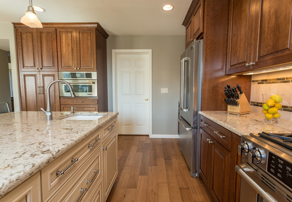 Large transitional l-shaped medium tone wood floor and brown floor eat-in kitchen photo in Denver with raised-panel cabinets, medium tone wood cabinets, granite countertops, beige backsplash, stone tile backsplash, stainless steel appliances, an island and an undermount sink
