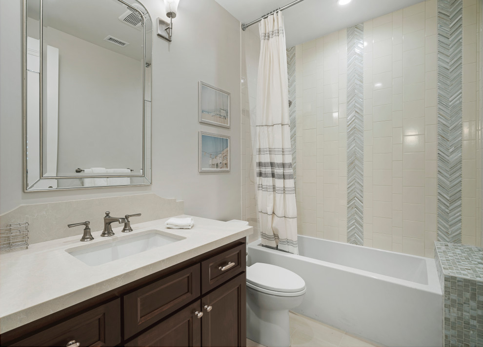 Photo of a small beach style kids bathroom in Los Angeles with recessed-panel cabinets, brown cabinets, an alcove tub, an alcove shower, a one-piece toilet, beige tile, porcelain tile, beige walls, pebble tile floors, an undermount sink, engineered quartz benchtops, beige floor, a shower curtain, beige benchtops, a shower seat, a single vanity and a built-in vanity.