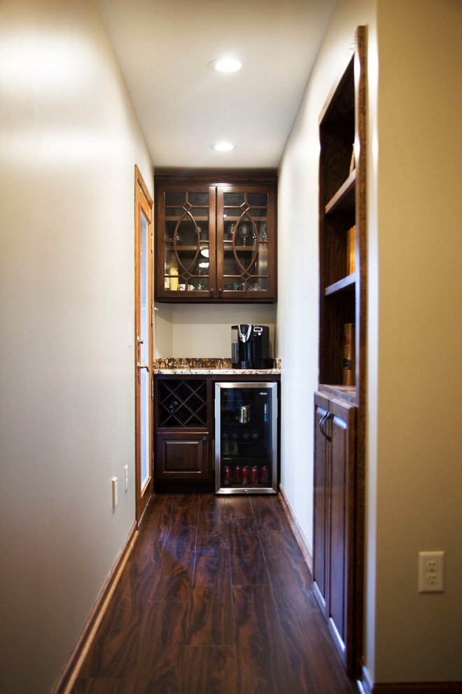 Photo of a small contemporary single-wall home bar in Milwaukee with no sink, raised-panel cabinets, dark wood cabinets, granite benchtops, dark hardwood floors and brown floor.