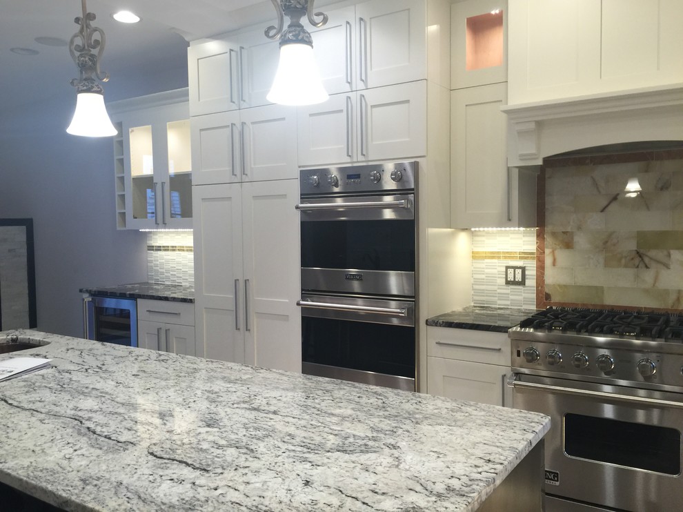 Mid-sized transitional u-shaped light wood floor and beige floor eat-in kitchen photo in Boston with recessed-panel cabinets, white cabinets, stainless steel appliances, a farmhouse sink, granite countertops, beige backsplash, stone tile backsplash, an island and multicolored countertops