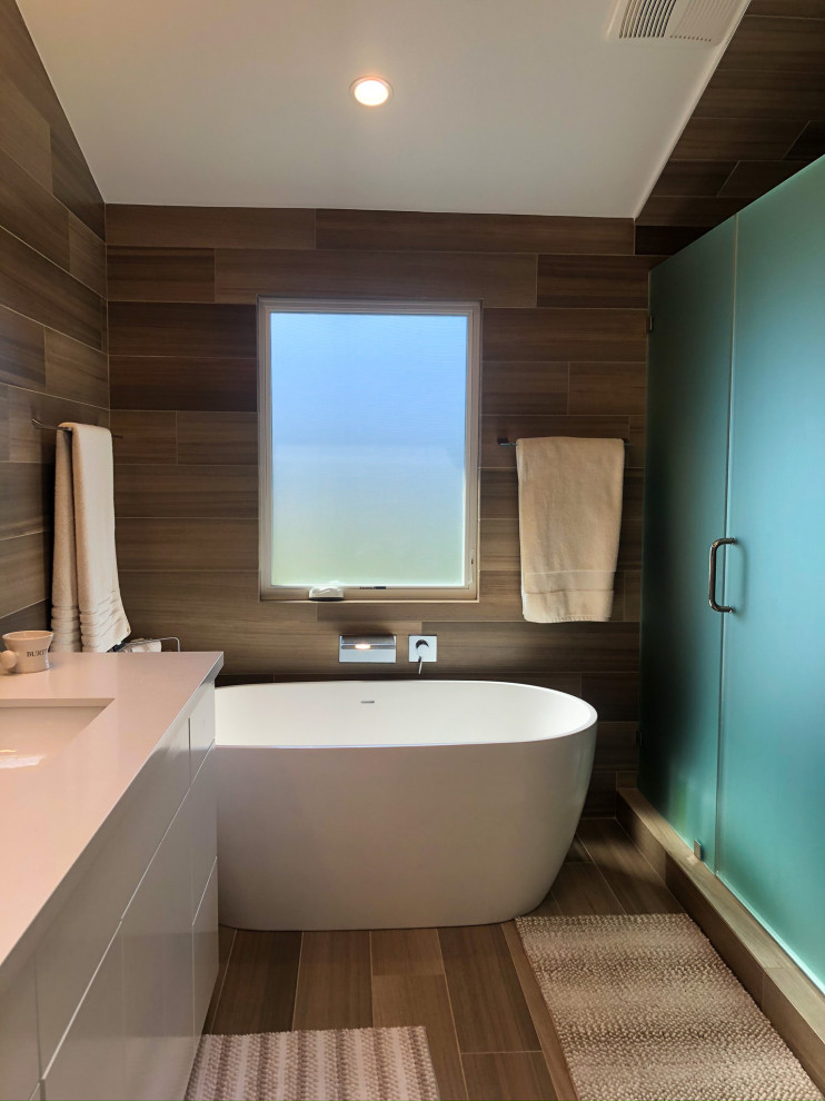 Photo of a mid-sized modern master bathroom in Los Angeles with flat-panel cabinets, white cabinets, a freestanding tub, an alcove shower, a one-piece toilet, brown tile, brown walls, an undermount sink, quartzite benchtops, brown floor, a hinged shower door, white benchtops, an enclosed toilet, a double vanity, a built-in vanity, wood walls, porcelain tile and porcelain floors.