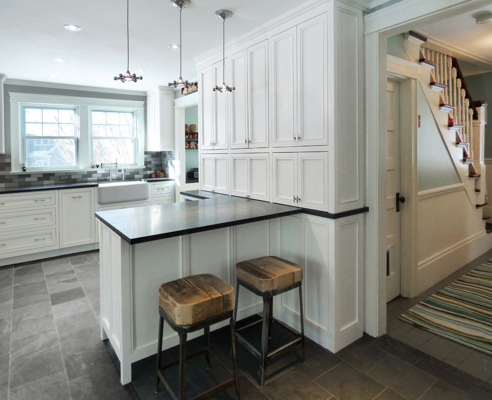 Inspiration for a mid-sized transitional l-shaped kitchen in Boston with a farmhouse sink, recessed-panel cabinets, white cabinets, granite benchtops, metallic splashback, metal splashback, stainless steel appliances, slate floors and a peninsula.