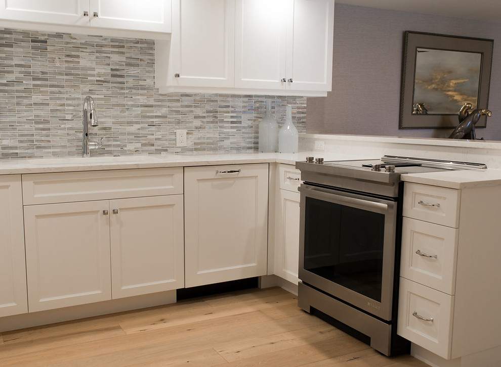 Example of a mid-sized transitional u-shaped light wood floor and beige floor enclosed kitchen design in Miami with an undermount sink, shaker cabinets, white cabinets, solid surface countertops, multicolored backsplash, matchstick tile backsplash, stainless steel appliances and no island