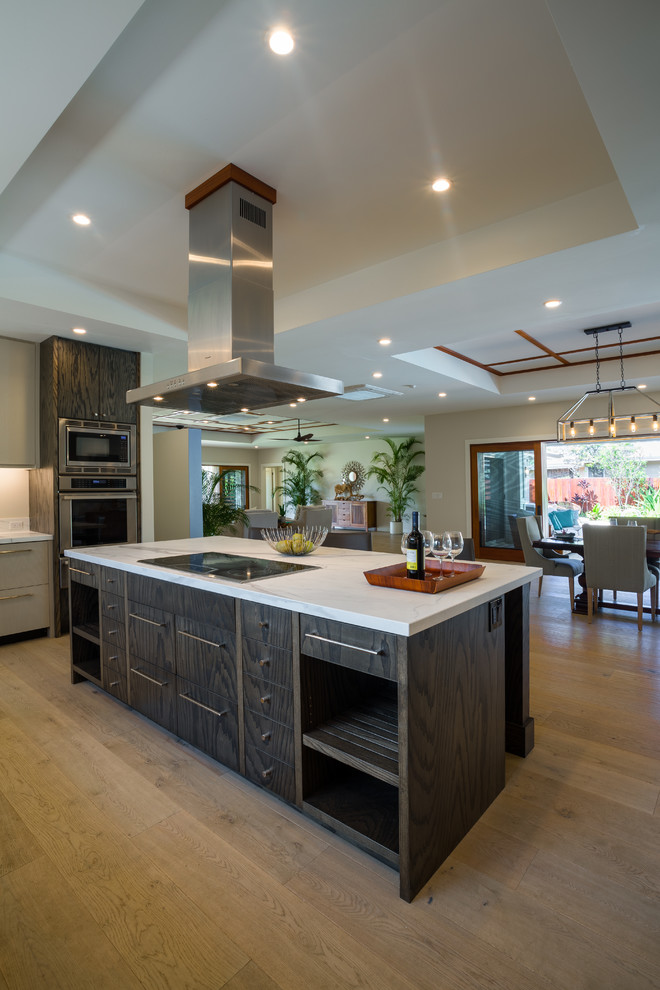 Photo of a large beach style u-shaped eat-in kitchen in Hawaii with an undermount sink, flat-panel cabinets, dark wood cabinets, solid surface benchtops, white splashback, stone slab splashback, stainless steel appliances, light hardwood floors, with island, beige floor and white benchtop.