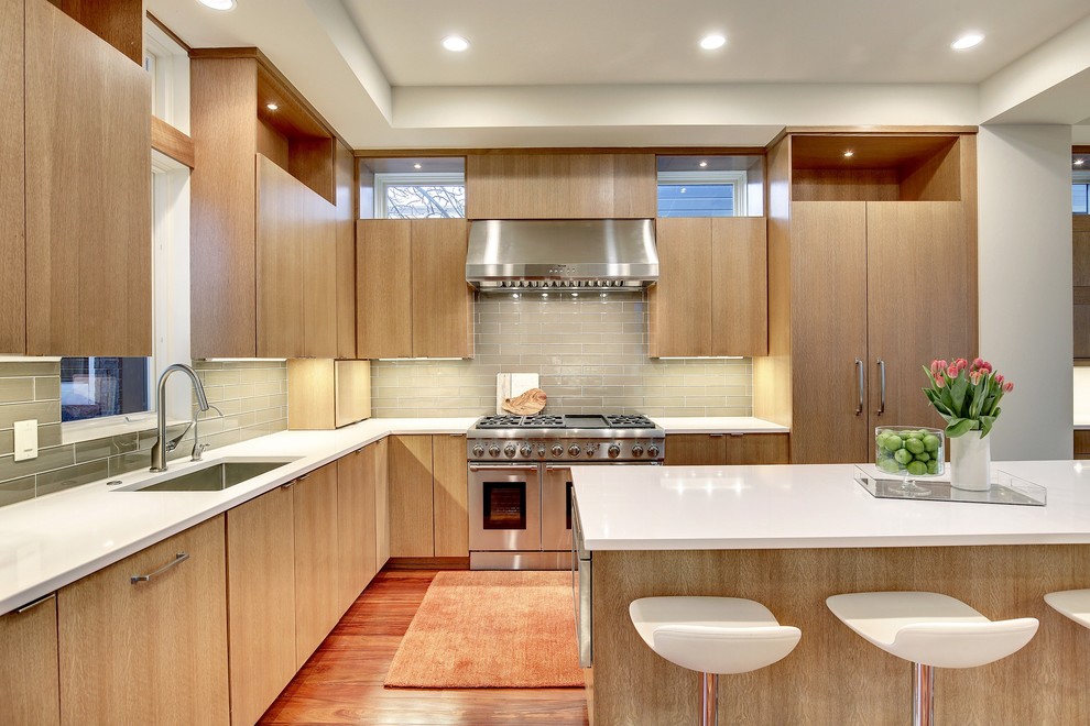 Photo of a mid-sized modern l-shaped open plan kitchen in Minneapolis with a single-bowl sink, flat-panel cabinets, medium wood cabinets, solid surface benchtops, grey splashback, glass tile splashback, panelled appliances, medium hardwood floors and with island.