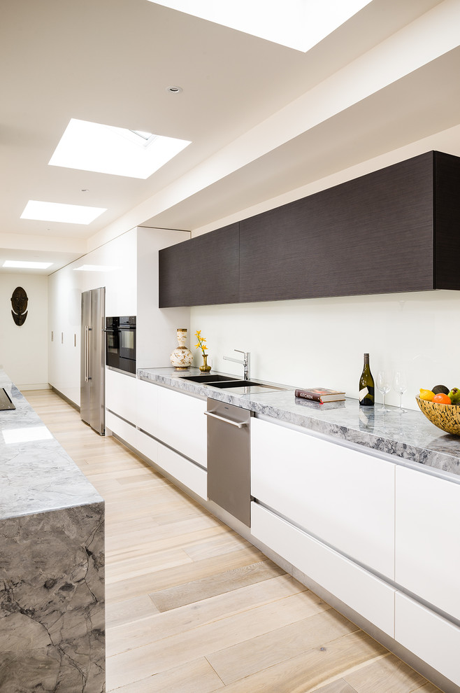 This is an example of an expansive modern l-shaped eat-in kitchen in Melbourne with an undermount sink, flat-panel cabinets, dark wood cabinets, marble benchtops, white splashback, glass sheet splashback, stainless steel appliances and with island.