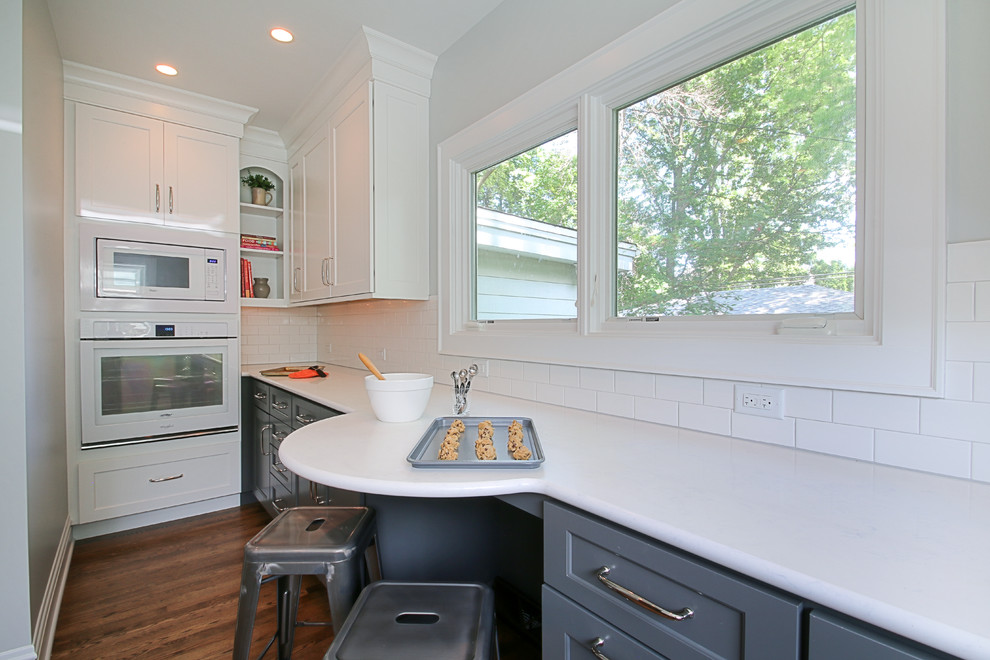 Example of a small transitional u-shaped dark wood floor enclosed kitchen design in Chicago with an undermount sink, shaker cabinets, white cabinets, quartz countertops, white backsplash, subway tile backsplash, white appliances and no island