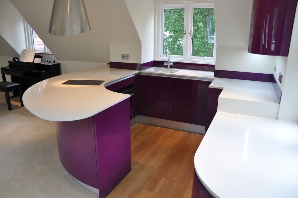 Inspiration for a mid-sized contemporary u-shaped open plan kitchen in Kent with a drop-in sink, flat-panel cabinets, purple cabinets, quartzite benchtops, glass sheet splashback, black appliances, light hardwood floors, a peninsula, brown floor and white benchtop.