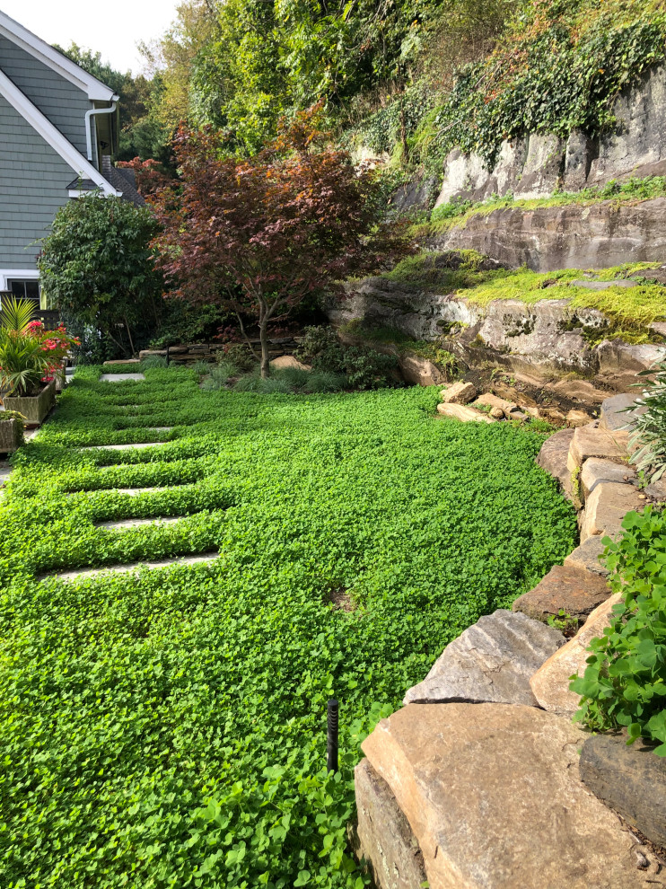 Small transitional backyard full sun xeriscape in New York with a retaining wall and river rock for summer.
