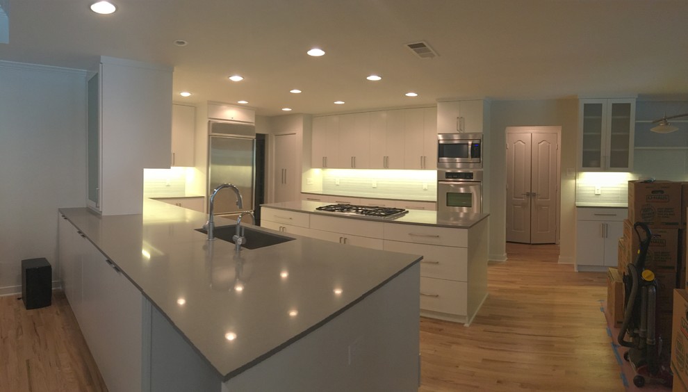 Example of a large transitional u-shaped light wood floor kitchen design in Dallas with an undermount sink, flat-panel cabinets, white cabinets, quartz countertops, gray backsplash, glass tile backsplash, stainless steel appliances and an island
