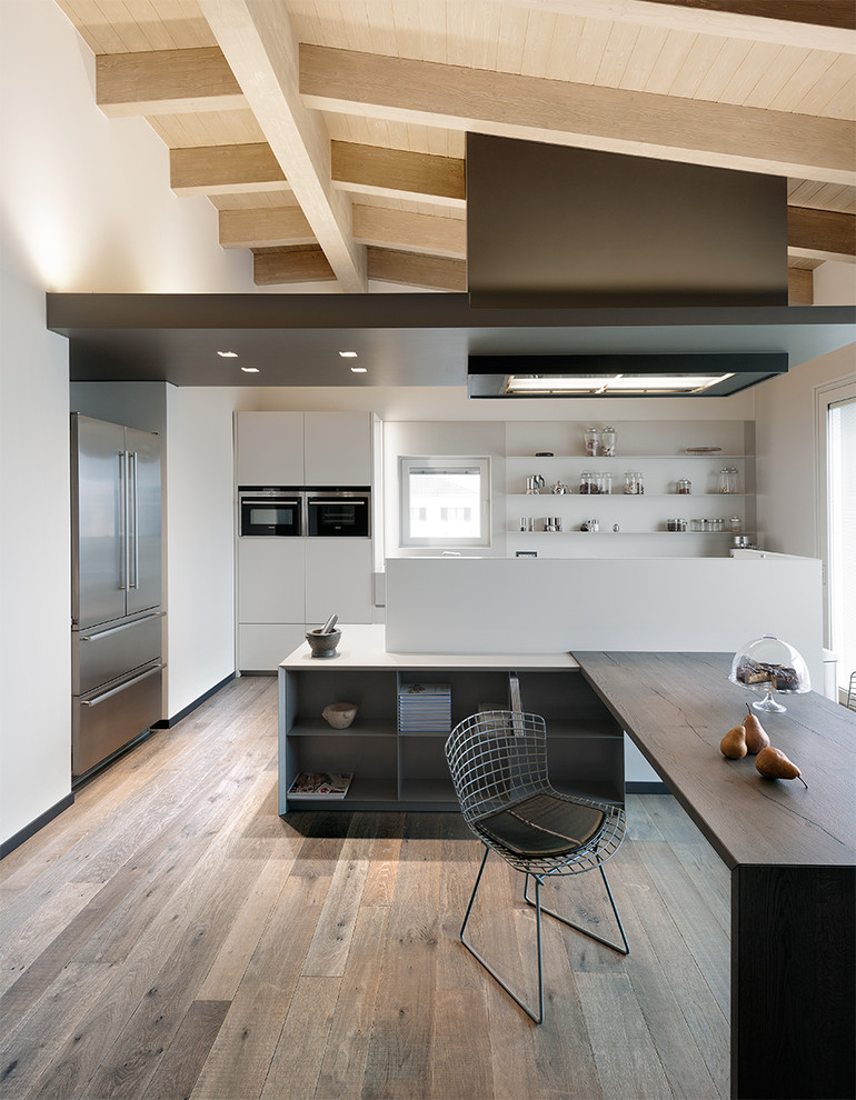 Inspiration for a large contemporary u-shaped eat-in kitchen in Milan with white cabinets, white splashback, stainless steel appliances, light hardwood floors, flat-panel cabinets and with island.