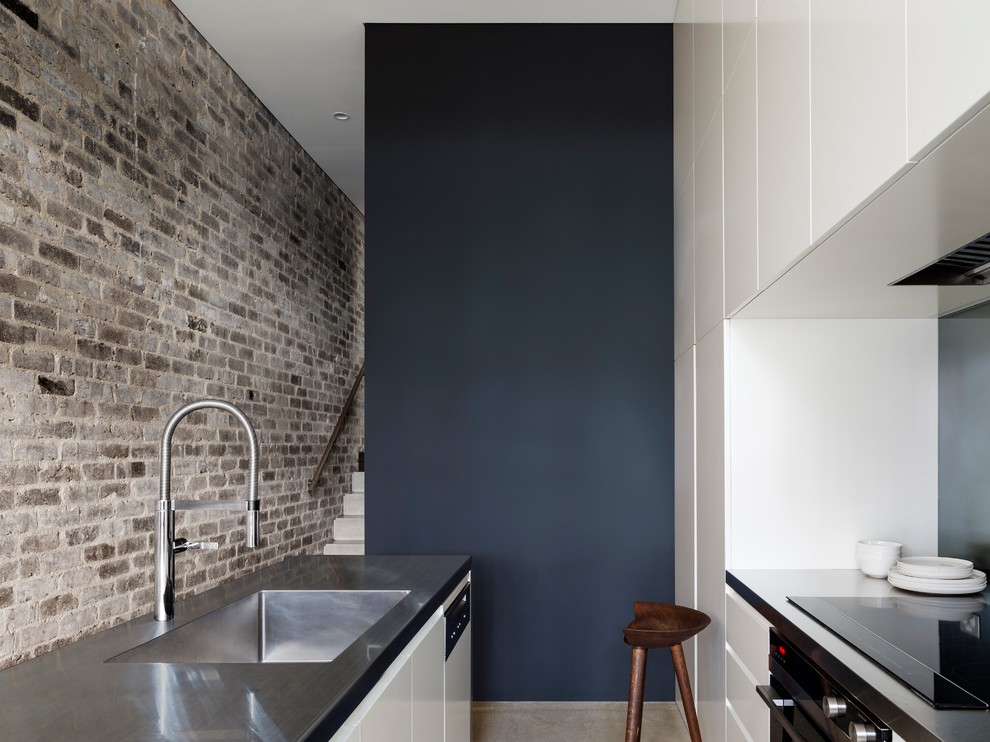 Inspiration for a small industrial single-wall eat-in kitchen in Sydney with a single-bowl sink, flat-panel cabinets, white cabinets, stainless steel benchtops, metallic splashback, mirror splashback, stainless steel appliances, concrete floors and with island.