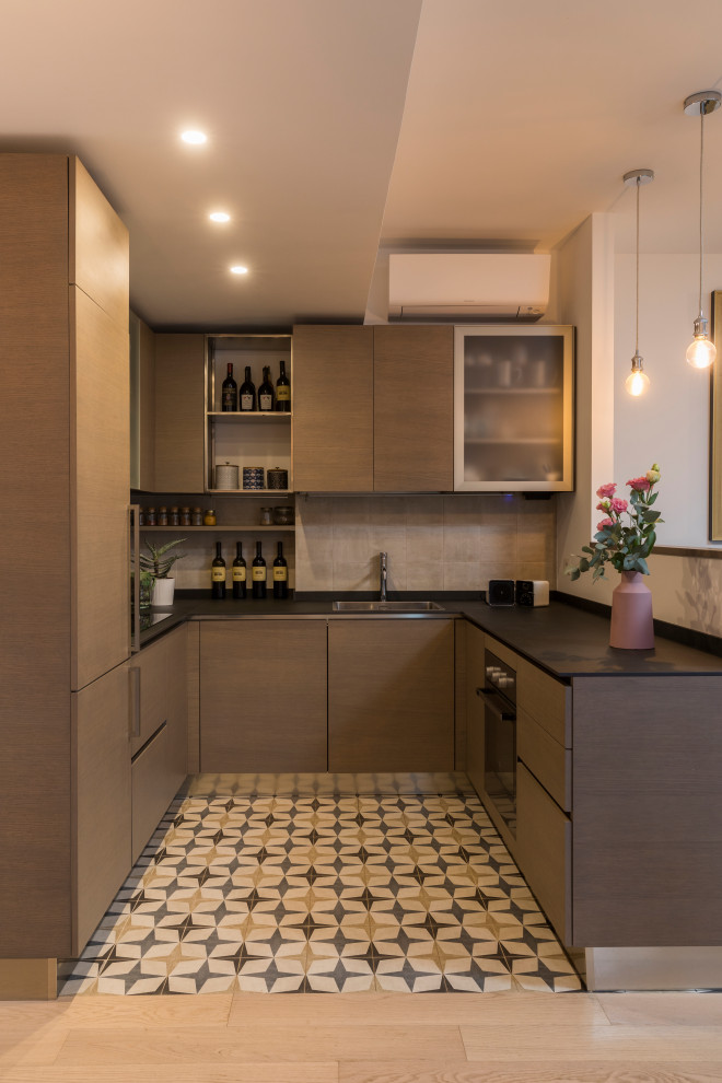 This is an example of a small contemporary u-shaped kitchen in Rome with a double-bowl sink, flat-panel cabinets, medium wood cabinets, beige splashback, porcelain floors, no island, multi-coloured floor and black benchtop.
