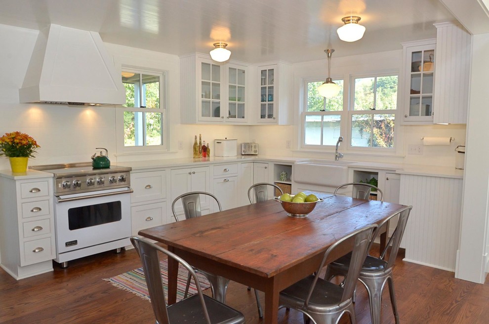 Photo of a small country u-shaped eat-in kitchen in Other with a farmhouse sink, beaded inset cabinets, white cabinets, quartz benchtops, white splashback, white appliances, medium hardwood floors and no island.