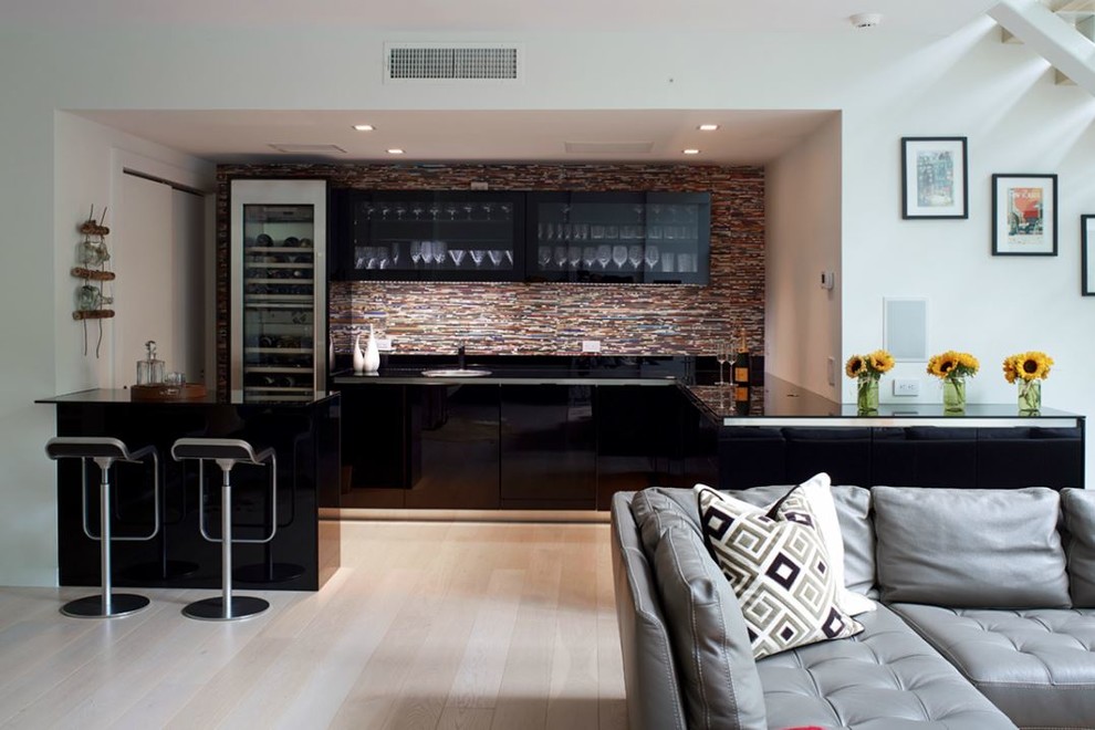 Mid-sized modern galley seated home bar in New York with a drop-in sink, flat-panel cabinets, black cabinets, solid surface benchtops, multi-coloured splashback, light hardwood floors and brown floor.