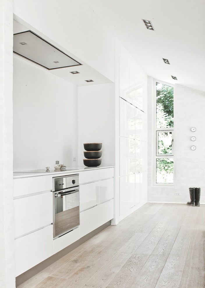 Photo of a mid-sized scandinavian single-wall separate kitchen in London with flat-panel cabinets, white cabinets, white splashback, stainless steel appliances, light hardwood floors, no island and laminate benchtops.