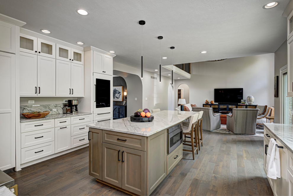 Photo of a contemporary galley open plan kitchen in Indianapolis with shaker cabinets, white cabinets, granite worktops, white splashback, granite splashback, stainless steel appliances, dark hardwood flooring, an island, white worktops and brown floors.