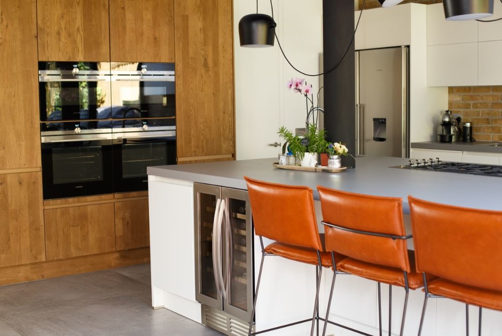 Photo of a mid-sized eclectic single-wall kitchen in London with a drop-in sink, flat-panel cabinets, white cabinets, concrete benchtops, beige splashback, brick splashback, stainless steel appliances, porcelain floors, with island, grey floor and grey benchtop.