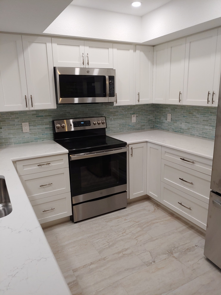 This is an example of a small beach style u-shaped eat-in kitchen in Tampa with an undermount sink, shaker cabinets, white cabinets, quartz benchtops, green splashback, glass tile splashback, stainless steel appliances, porcelain floors, no island, beige floor and white benchtop.
