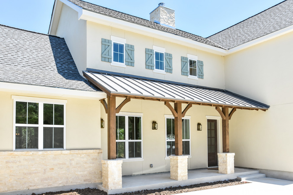 Photo of a large country two-storey stucco beige house exterior in Austin with a gable roof and a shingle roof.