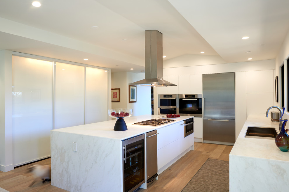 Mid-sized contemporary l-shaped eat-in kitchen in San Francisco with a drop-in sink, flat-panel cabinets, white cabinets, marble benchtops, white splashback, marble splashback, stainless steel appliances, light hardwood floors, with island, white benchtop and beige floor.