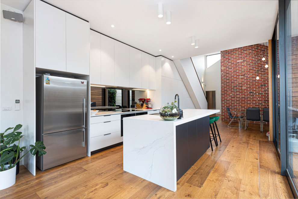 Contemporary eat-in kitchen in Melbourne with an undermount sink, white cabinets, quartz benchtops, grey splashback, mirror splashback, stainless steel appliances, light hardwood floors, with island and white benchtop.