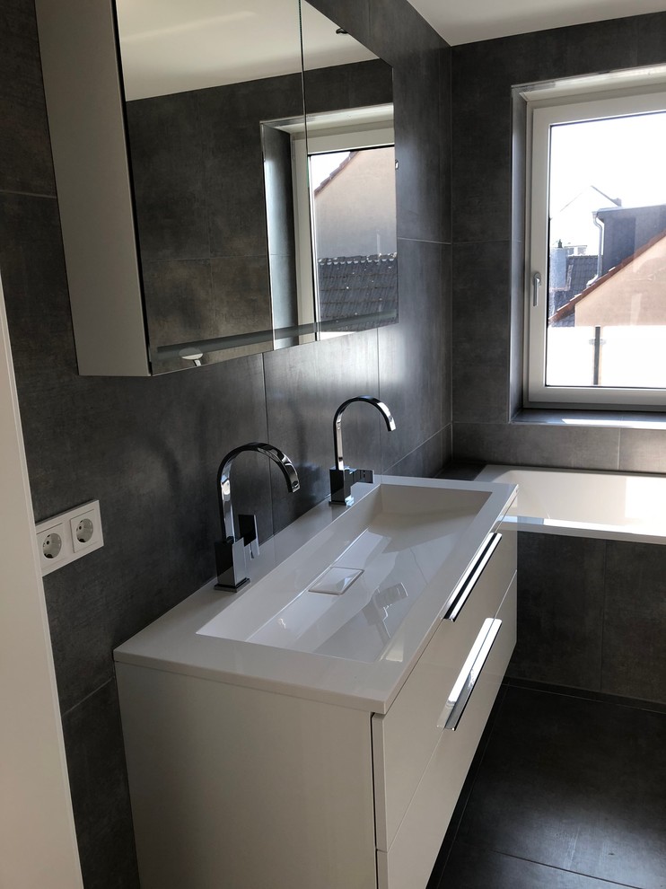 Mid-sized contemporary 3/4 bathroom in Cologne with glass-front cabinets, white cabinets, a drop-in tub, an open shower, a two-piece toilet, gray tile, stone tile, cement tiles, an integrated sink, solid surface benchtops, grey floor, an open shower, white benchtops and grey walls.