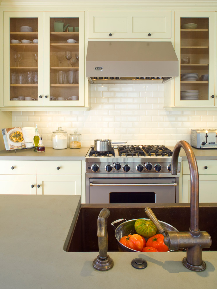 This is an example of a traditional kitchen in San Francisco with a farmhouse sink, glass-front cabinets, yellow cabinets, white splashback, ceramic splashback, stainless steel appliances and quartz benchtops.