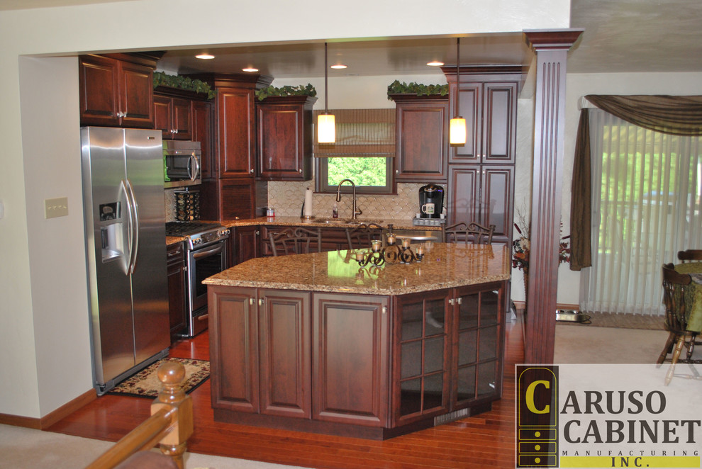 Small elegant l-shaped medium tone wood floor eat-in kitchen photo with a double-bowl sink, raised-panel cabinets, dark wood cabinets, beige backsplash, ceramic backsplash, stainless steel appliances and an island