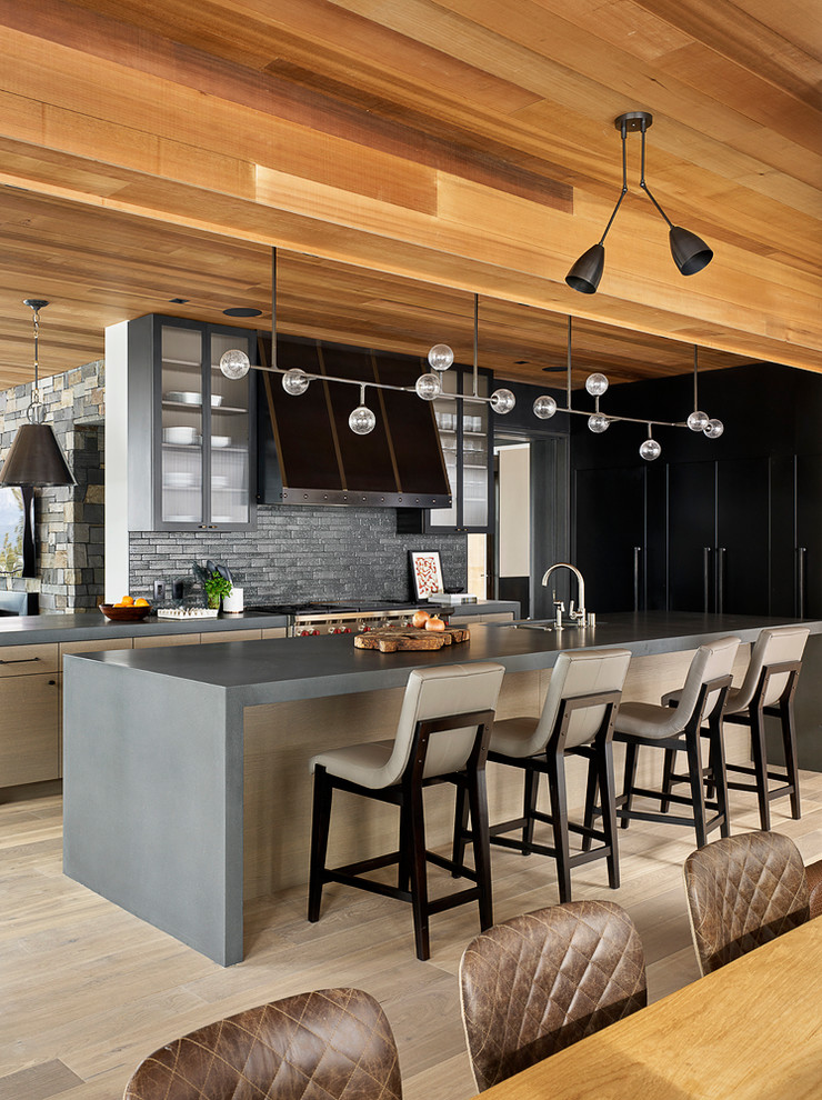 This is an example of a contemporary galley open plan kitchen in San Francisco with an undermount sink, flat-panel cabinets, light wood cabinets, concrete benchtops, grey splashback, stone tile splashback, panelled appliances, light hardwood floors, with island, beige floor and grey benchtop.