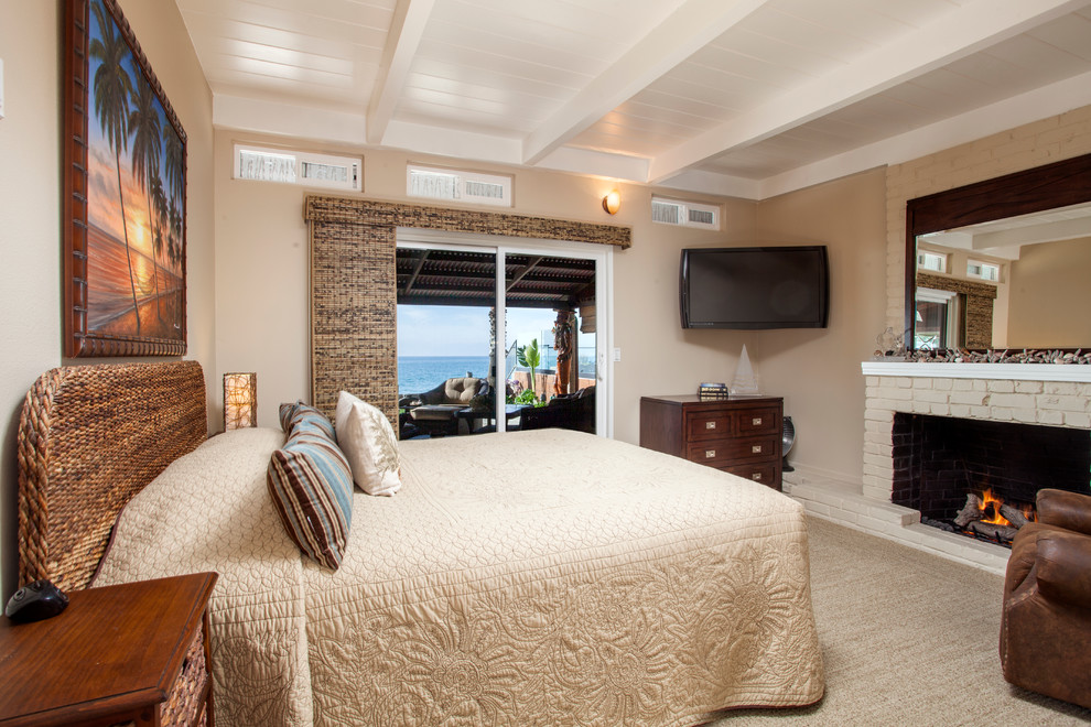 Design ideas for a large tropical master bedroom in Orange County with beige walls, carpet, a brick fireplace surround, a standard fireplace and beige floor.