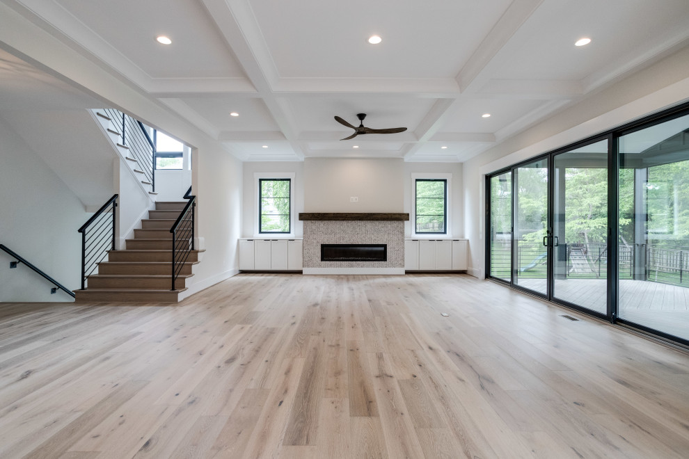 Large farmhouse open plan games room in DC Metro with light hardwood flooring, a standard fireplace, a tiled fireplace surround, a wall mounted tv and a coffered ceiling.