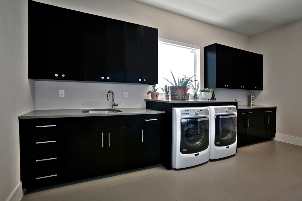 Large contemporary l-shaped utility room in Dallas with an undermount sink, flat-panel cabinets, solid surface benchtops, beige walls, ceramic floors, a side-by-side washer and dryer and black cabinets.