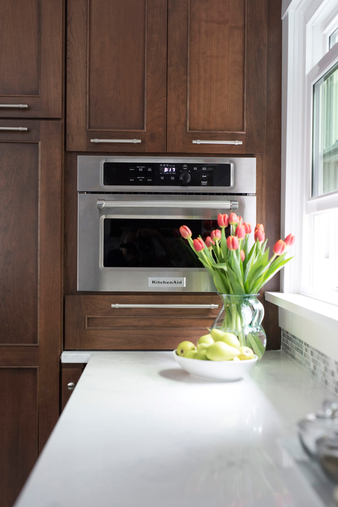 Mid-sized transitional u-shaped vinyl floor and multicolored floor kitchen photo with an undermount sink, shaker cabinets, brown cabinets, quartz countertops, gray backsplash, marble backsplash, stainless steel appliances, no island and white countertops