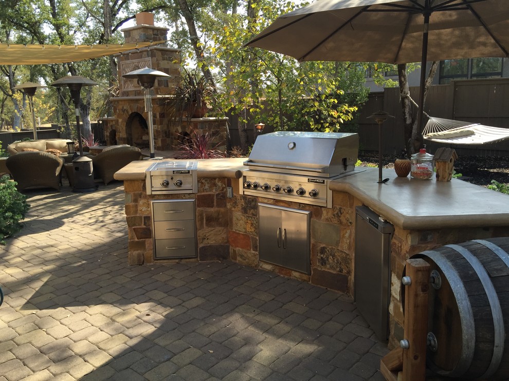 This is an example of a large country backyard patio in Sacramento with an outdoor kitchen, brick pavers and an awning.
