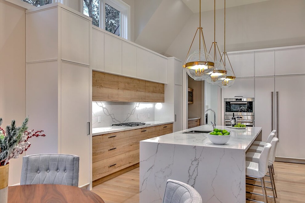 Inspiration for a large contemporary l-shaped eat-in kitchen in Toronto with flat-panel cabinets, light wood cabinets, marble benchtops, white splashback, marble splashback, stainless steel appliances, light hardwood floors, with island, beige floor, white benchtop and an undermount sink.