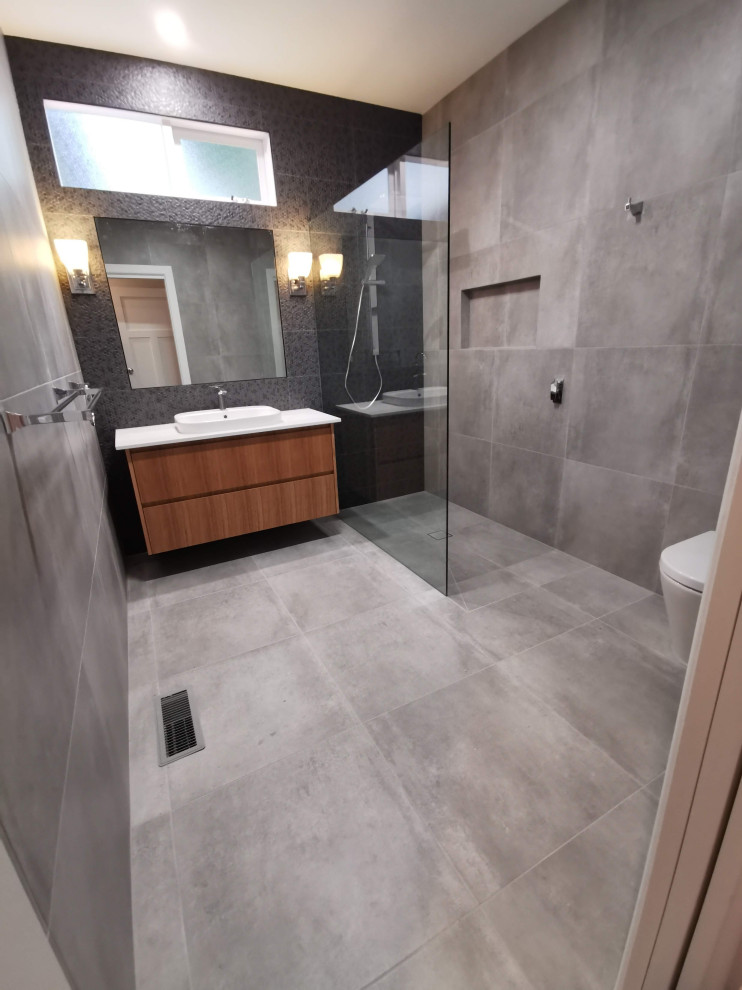 Design ideas for a medium sized classic ensuite bathroom in Melbourne with flat-panel cabinets, brown cabinets, a walk-in shower, a one-piece toilet, grey tiles, ceramic tiles, ceramic flooring, a vessel sink, engineered stone worktops, grey floors, an open shower, white worktops, a wall niche, a single sink and a floating vanity unit.