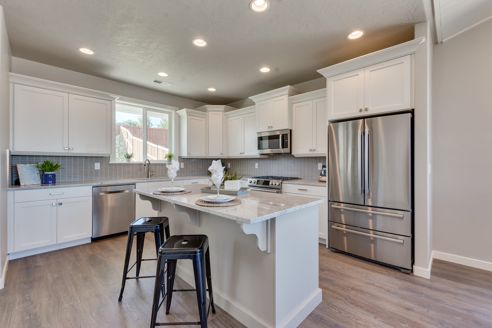 Design ideas for a mid-sized transitional u-shaped eat-in kitchen in Boise with an undermount sink, recessed-panel cabinets, white cabinets, quartz benchtops, grey splashback, ceramic splashback, stainless steel appliances, light hardwood floors, with island, brown floor and white benchtop.